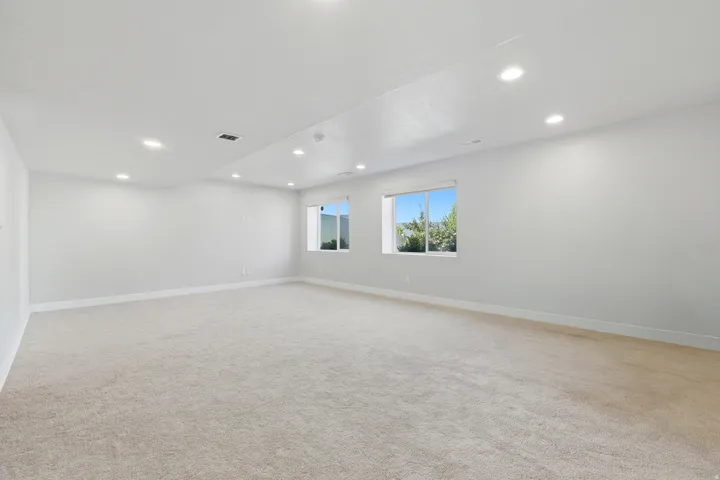 Spacious room with light-colored carpeting, recessed lighting, and multiple windows providing natural illumination