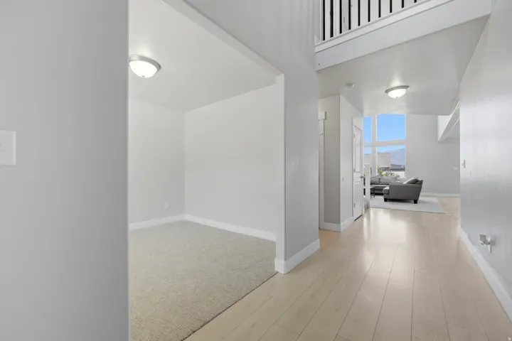 Light-toned wood-finish flooring extending into an open living area with large windows, complemented by a carpeted recessed space