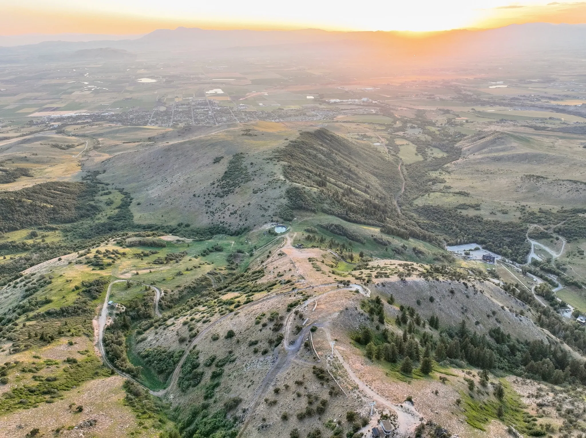Expansive mountain landscape featuring varied terrain, scattered trees, and distant urban development