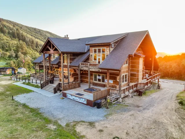 Multi-level log cabin-style exterior with extensive decking, a covered entry porch, and a gravel driveway