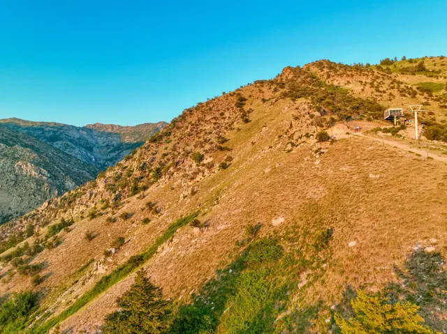 Mountainous terrain featuring a ski lift structure, a dirt path, and scattered evergreen trees