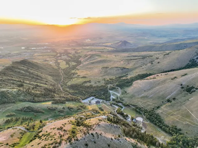 Sprawling landscape featuring expansive mountain ranges, green valleys, and distant structures under a vibrant sky