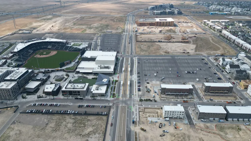 Aerial perspective showcasing a developing mixed-use community with a central baseball stadium, commercial buildings, and residential housing