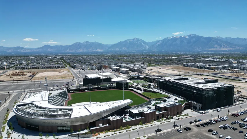 Aerial perspective showcasing a large sports stadium with a manicured green field, surrounded by an urban landscape