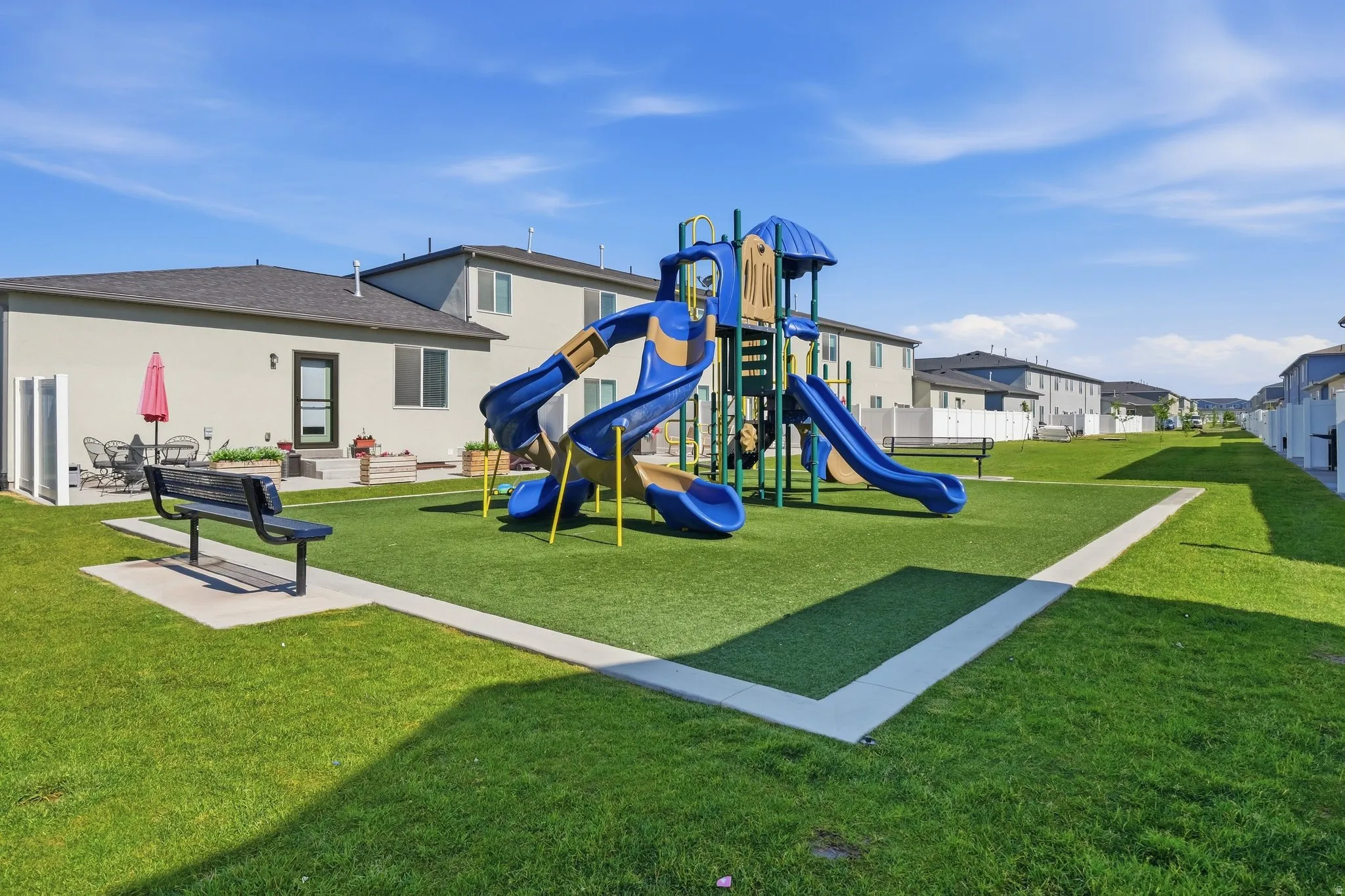 Community playground featuring a multi-level play structure with slides and climbing elements, surrounded by artificial turf and natural grass areas
