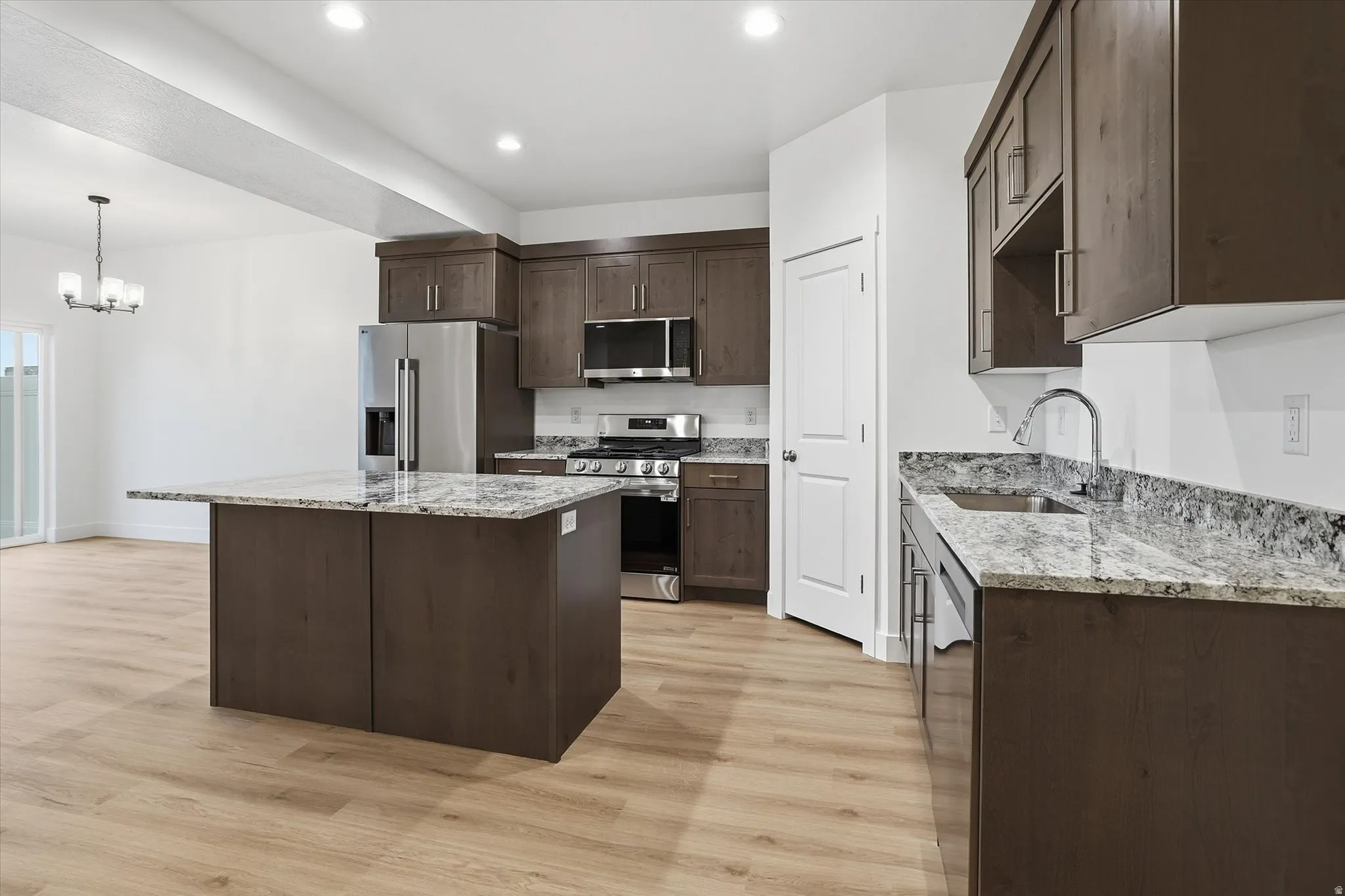 Open-concept kitchen featuring an island with a light-toned countertop, wood-finish cabinetry, stainless steel appliances, and wood-finish flooring