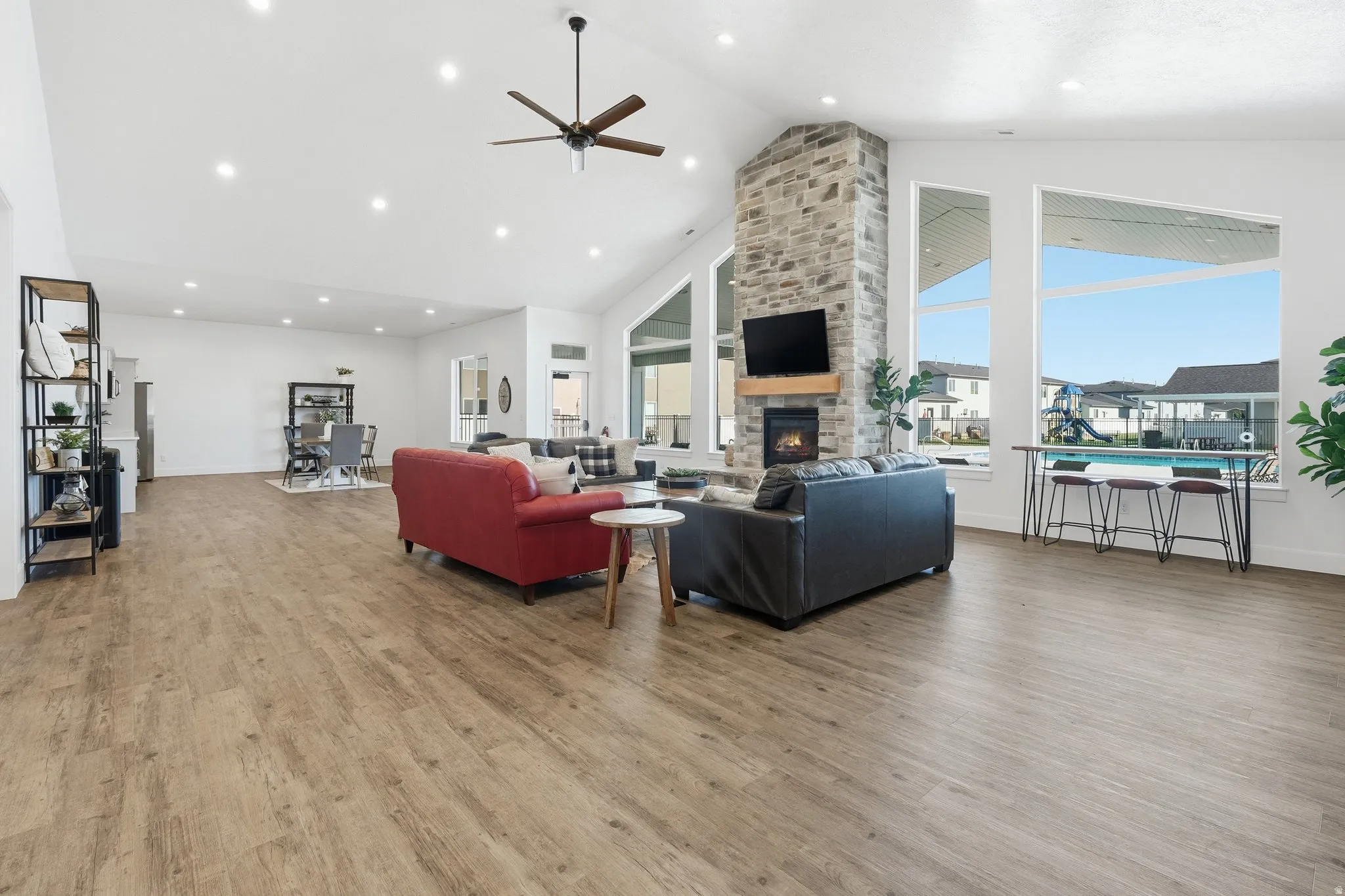 Spacious open-concept living area featuring vaulted ceilings, wood-finish flooring, and a stone-clad fireplace with an integrated media niche