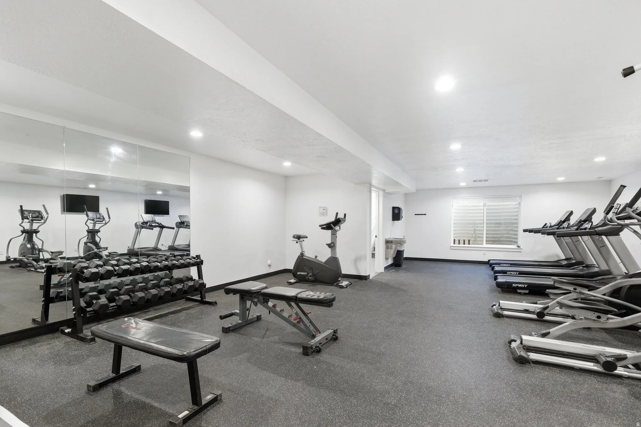 Dedicated fitness center featuring rubberized flooring, a full wall mirror, recessed lighting, and a window with horizontal blinds