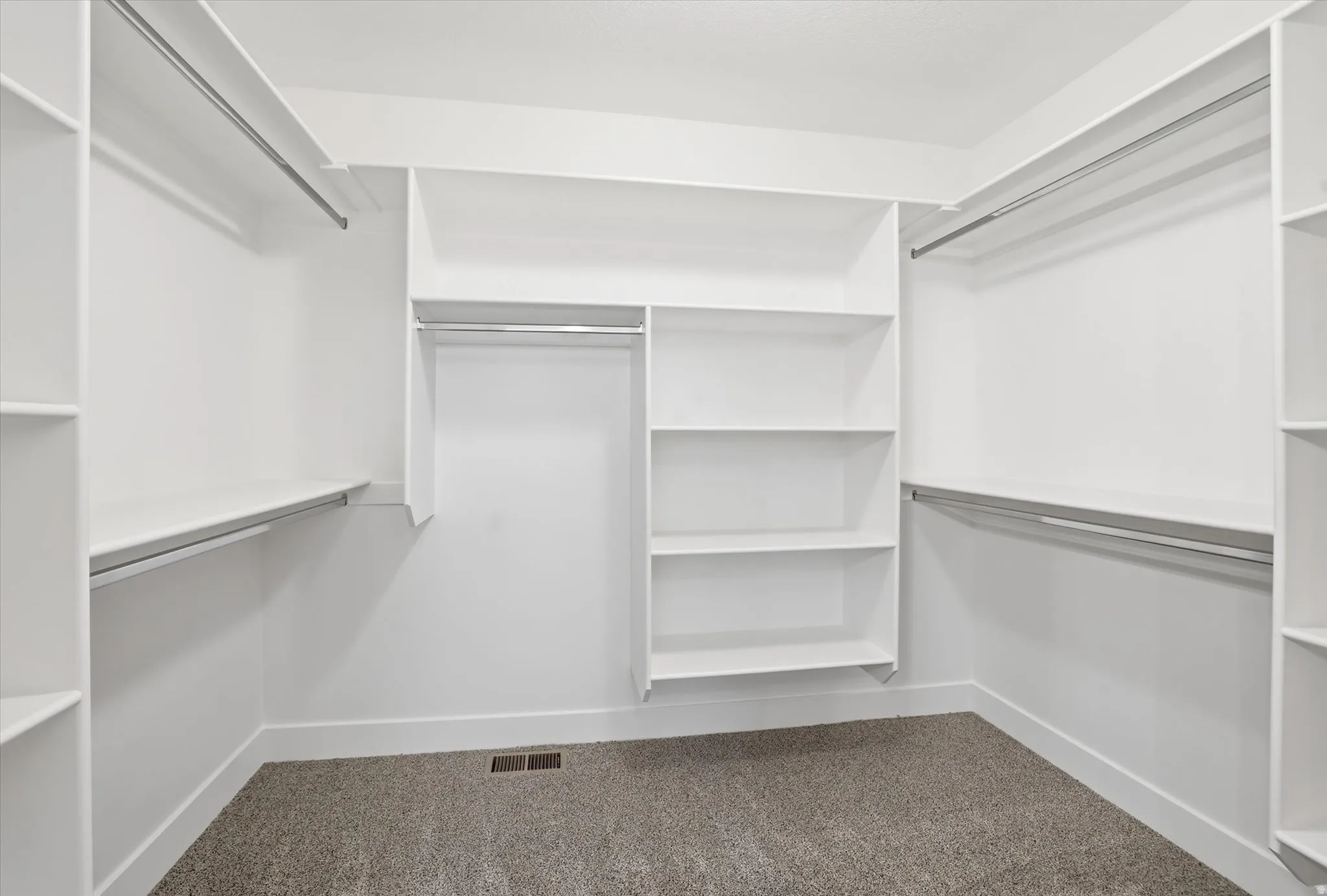 Walk-in closet featuring white built-in shelving, multiple hanging rods, and gray carpet flooring