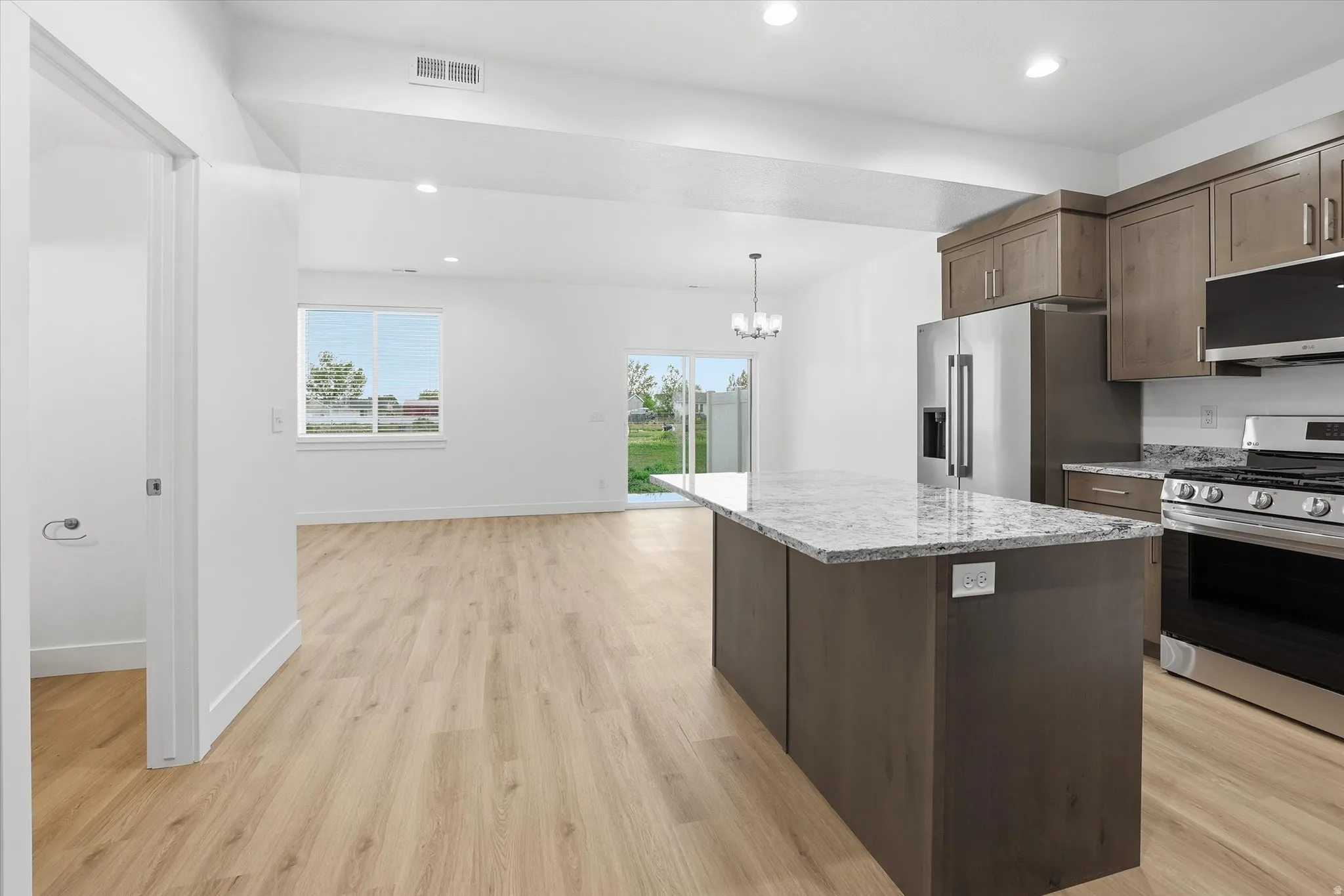 Kitchen featuring a large island with a light-toned countertop, stainless steel appliances, wood-finish cabinetry, and recessed lighting