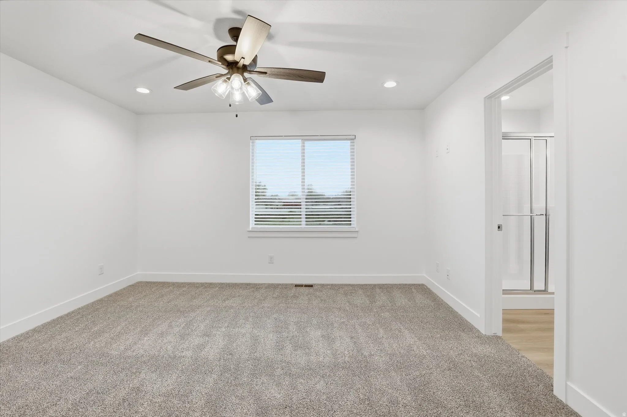 Spacious room featuring neutral carpeting, a ceiling fan with integrated lighting, and recessed overhead lights