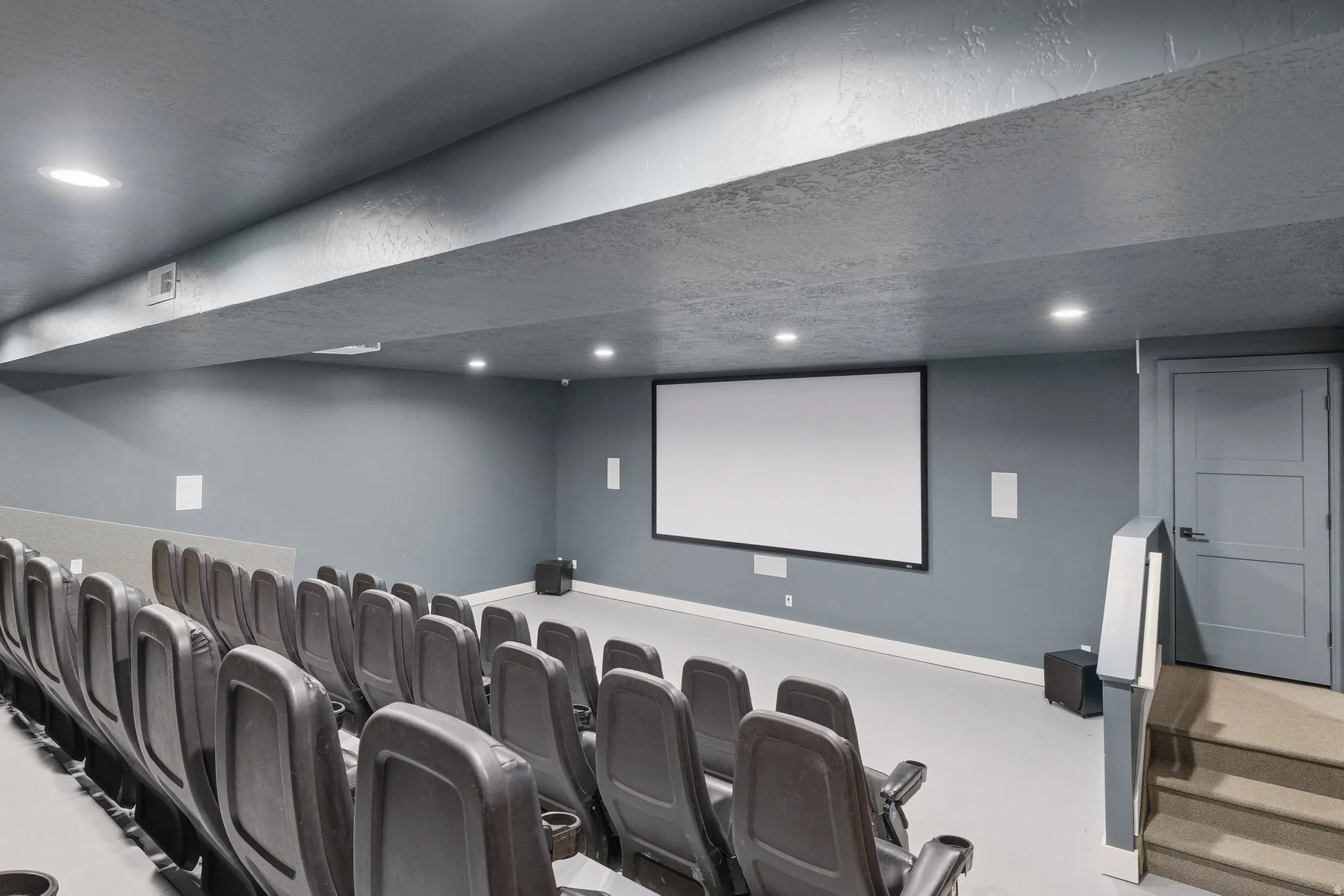 Dedicated home theater featuring tiered seating, a large projection screen, recessed lighting, integrated speakers, and a paneled interior door