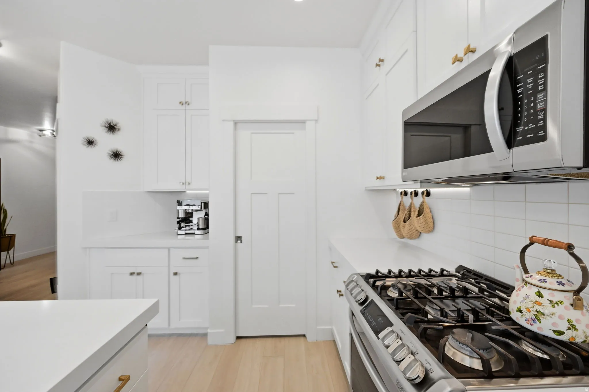Bright kitchen featuring white shaker cabinetry, stainless steel microwave, gas range with griddle, and white subway tile backsplash