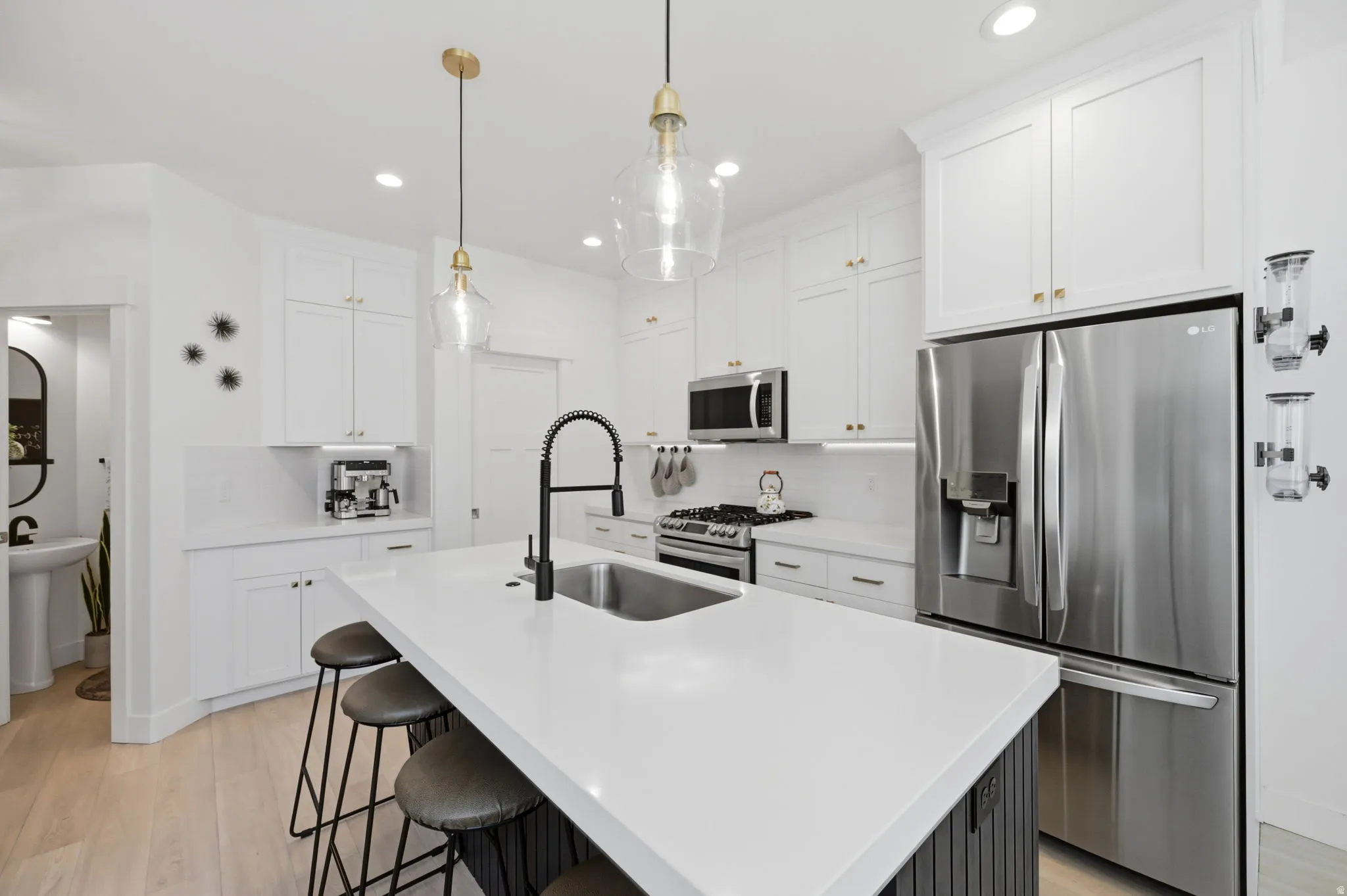 Kitchen featuring a large island with an undermount sink and matte black faucet, white shaker-style cabinetry with brass-finish hardware, stainless steel appliances