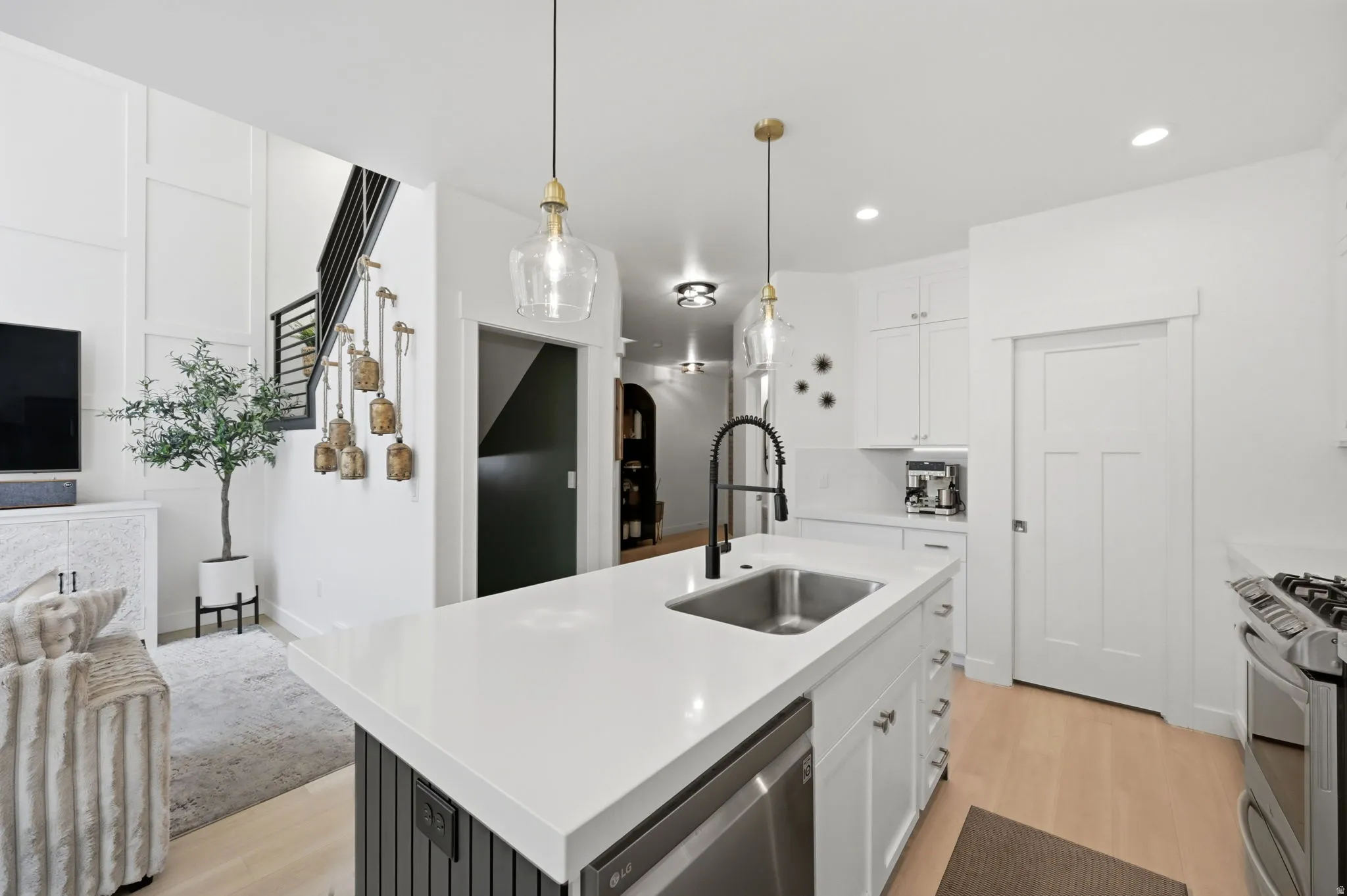 Kitchen island featuring a stainless steel sink with a matte black faucet, integrated dishwasher, and clear glass pendant lighting