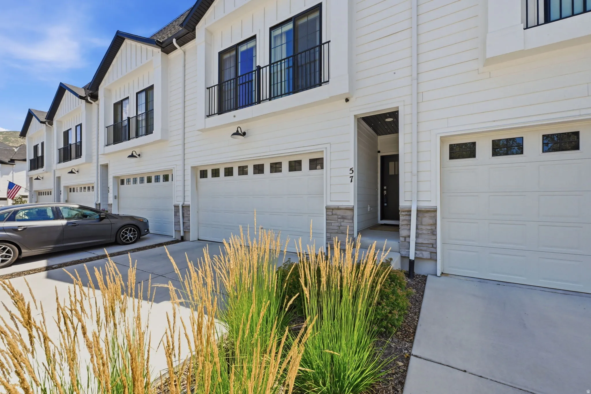 Contemporary townhome exterior featuring white siding, black trim accents, a double-car garage with transom windows, and a prominent front entry