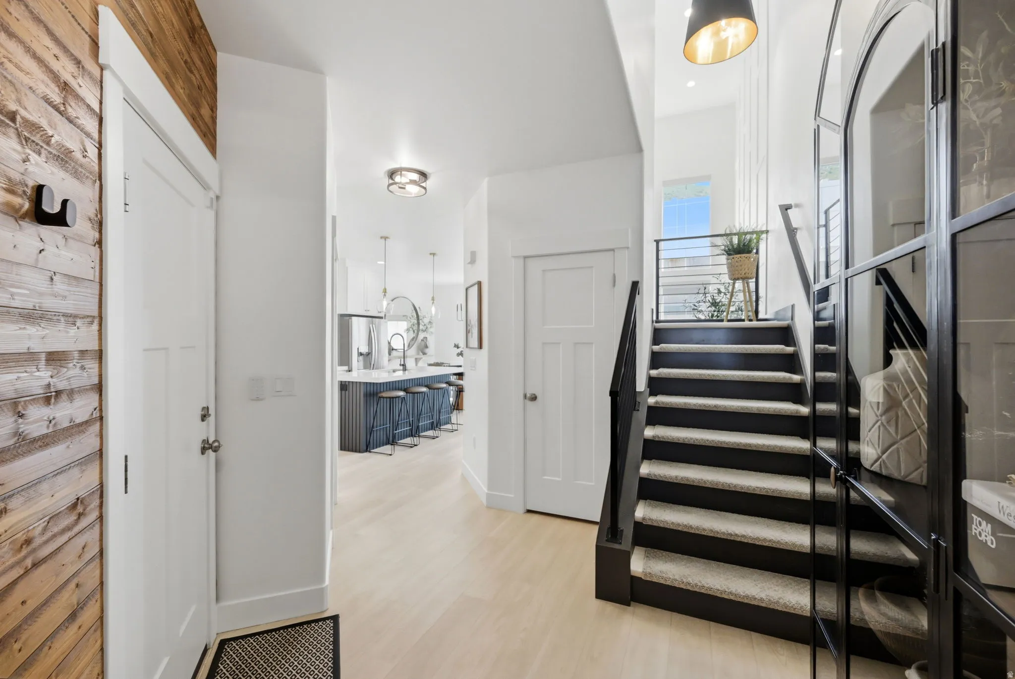 Bright entryway with wood-finish flooring, a contemporary staircase featuring carpeted treads and black railings, and a wood accent wall