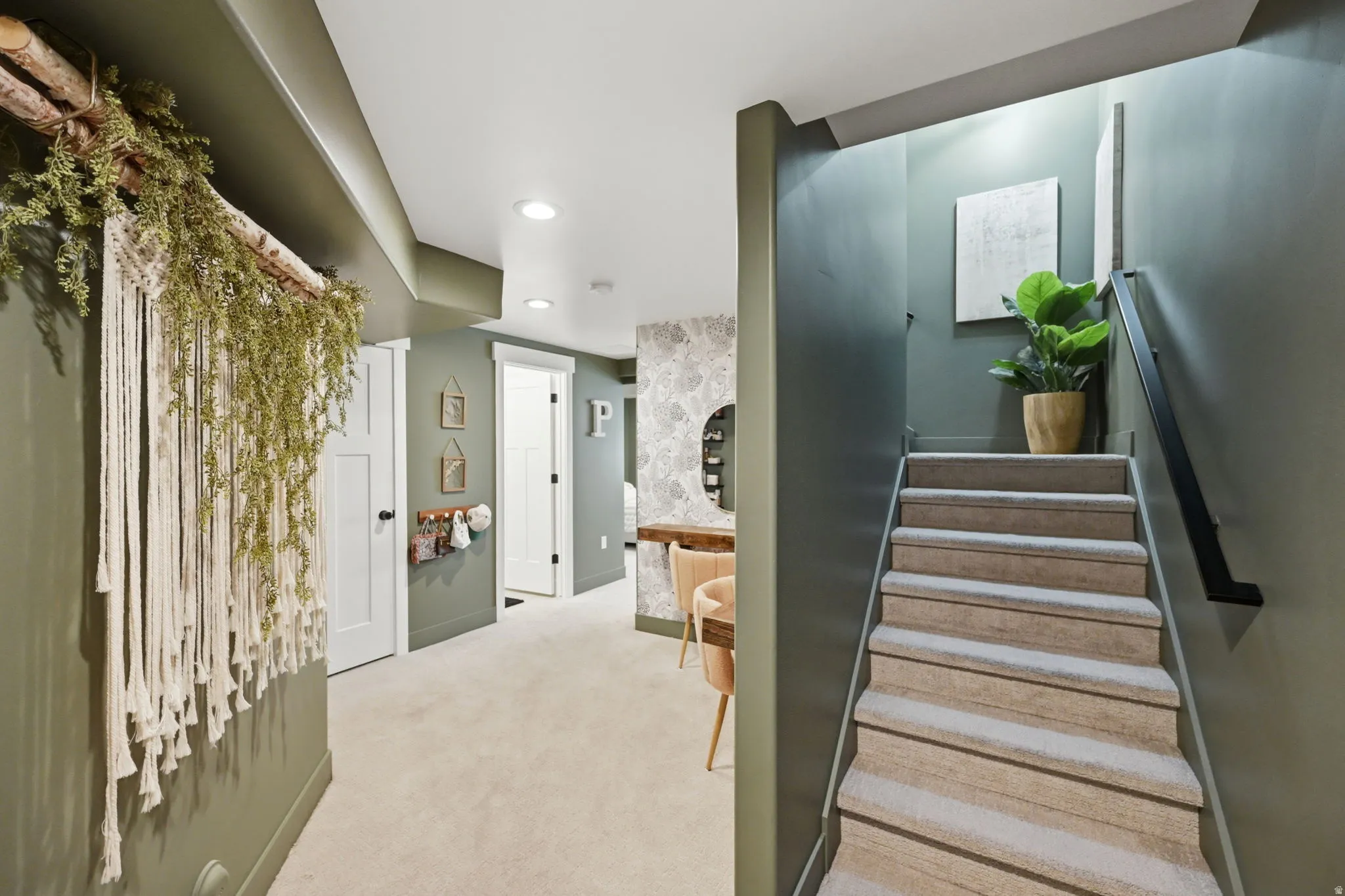Carpeted staircase with black metal handrail leading to a hallway with recessed lighting