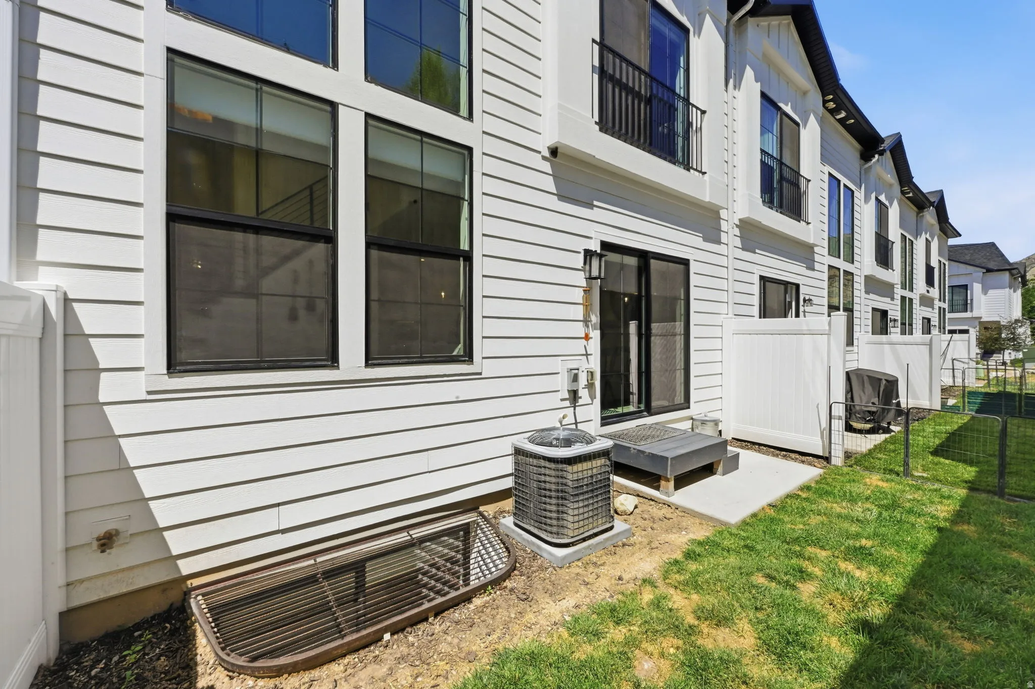 Contemporary exterior featuring white horizontal siding, black-framed windows, a sliding glass door, a private patio, and a compact lawn area
