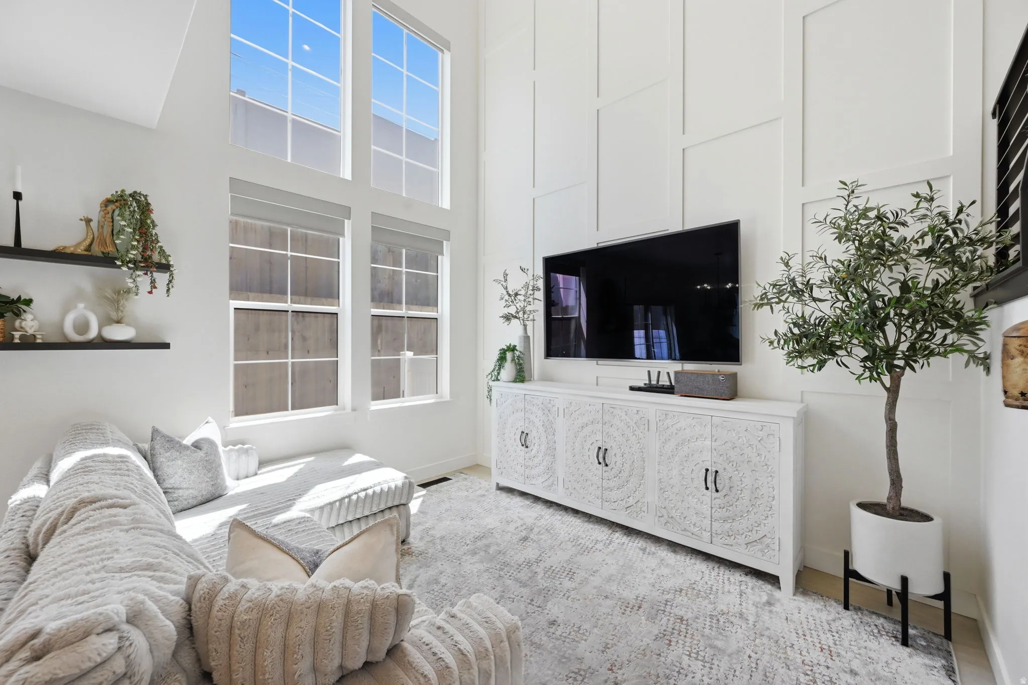 Two-story living area featuring tall windows with roller shades, and white panel accent wall
