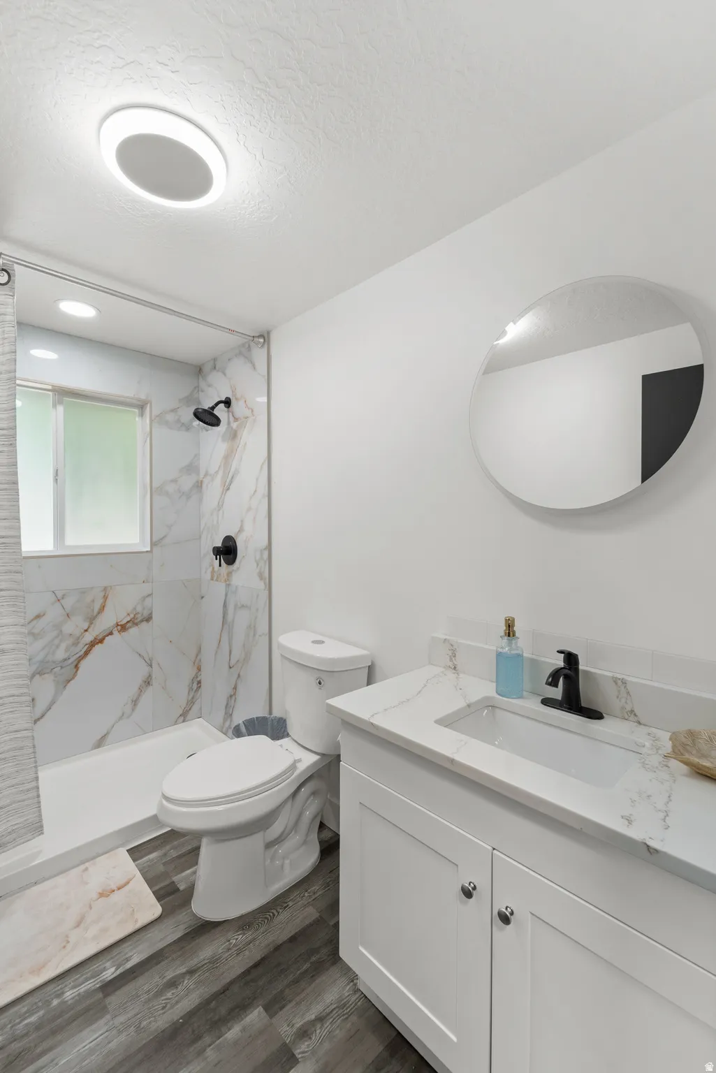 Bathroom featuring a white vanity with an integrated sink, black faucet, and a round frameless mirror