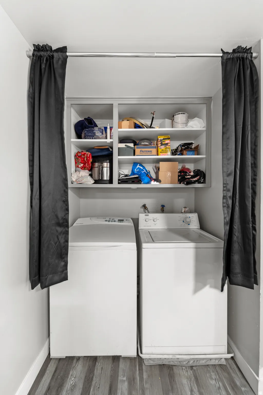 Dedicated laundry area featuring a built-in shelf unit, wood-finish flooring, white walls, and a clothes rod