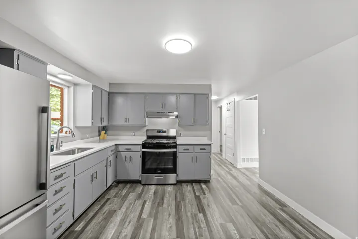 Kitchen featuring wood-finish flooring, light grey cabinetry with silver hardware, stainless steel appliances, a white sink with a gooseneck faucet, and white countertops