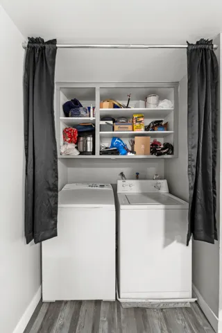 Dedicated laundry area featuring a built-in shelf unit, wood-finish flooring, white walls, and a clothes rod