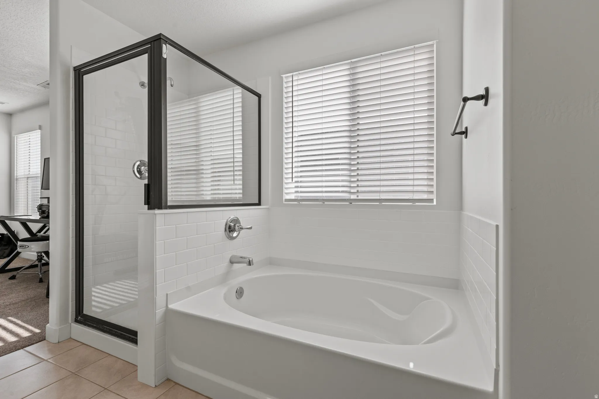 White soaking tub with subway tile surround, accompanied by a glass-enclosed shower with black framing