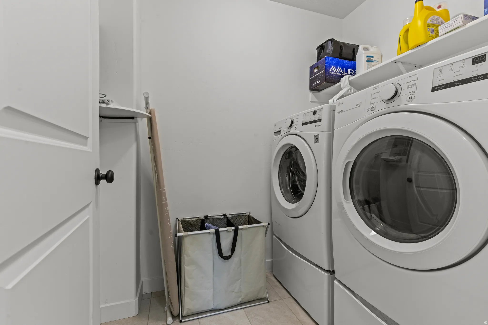Dedicated laundry area featuring front-loading appliances, a built-in shelf above the units, and light-toned flooring