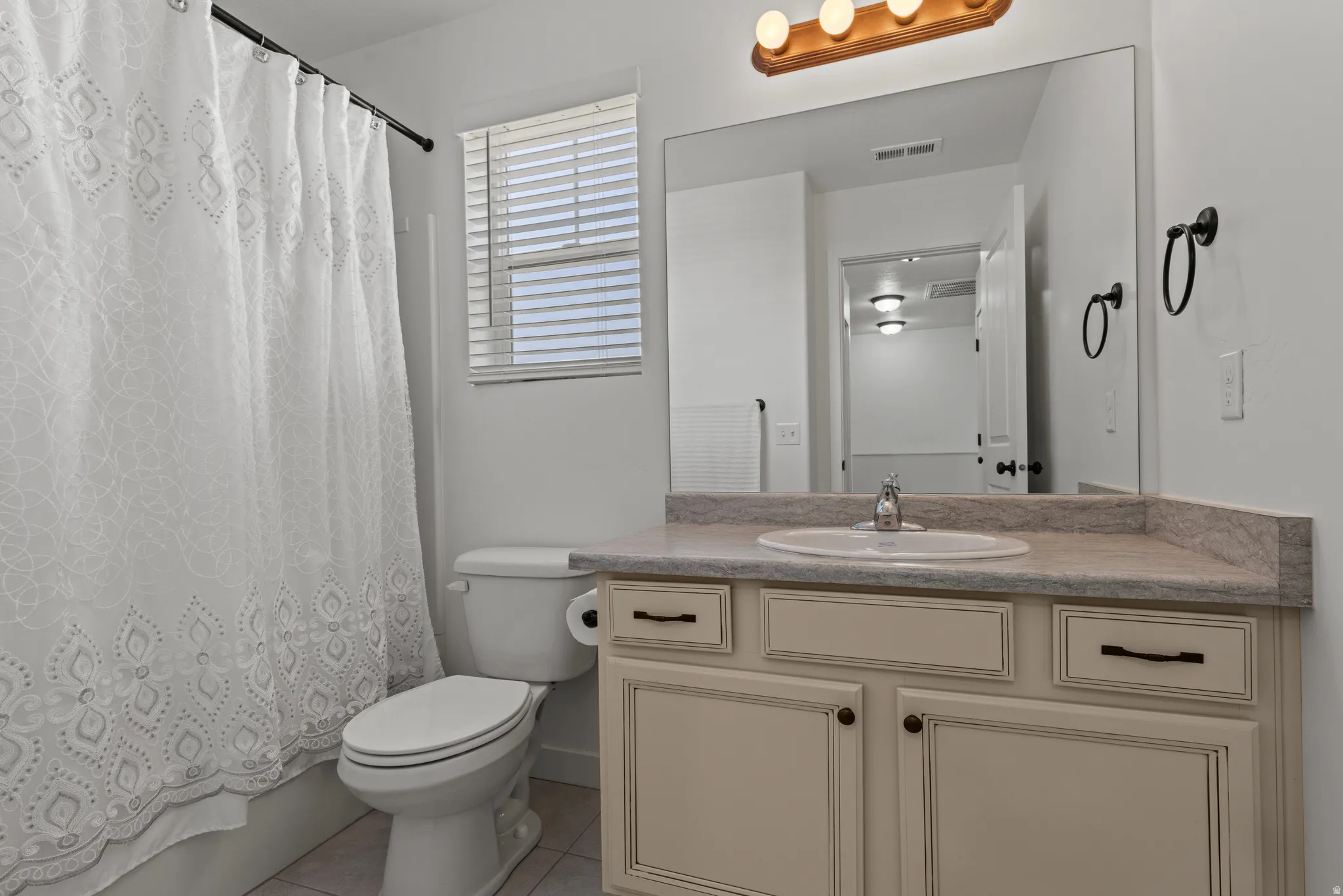 Bathroom featuring a neutral color palette, a vanity with a drop-in sink, wood-finish cabinetry, and a large mirror with a four-bulb light fixture
