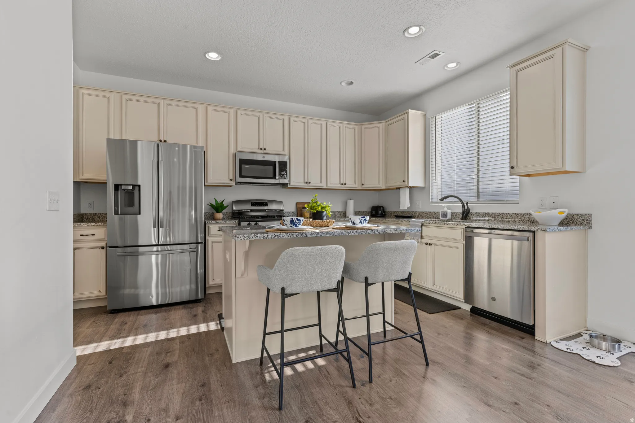 Kitchen featuring light wood-finish cabinetry, granite-style countertops, stainless steel appliances, a center island with built-in seating, and wood-finish flooring