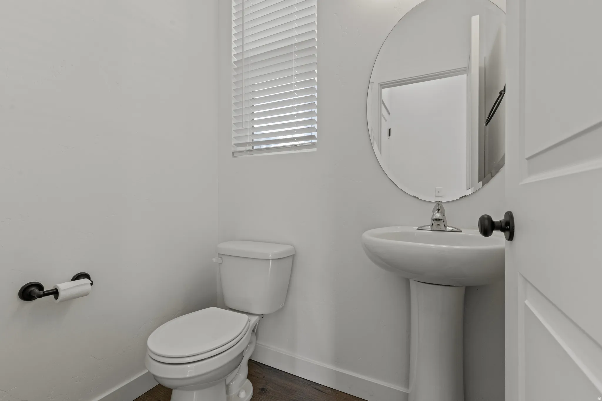 Powder room featuring a pedestal sink with a chrome faucet, an oval mirror, and wood-finish flooring
