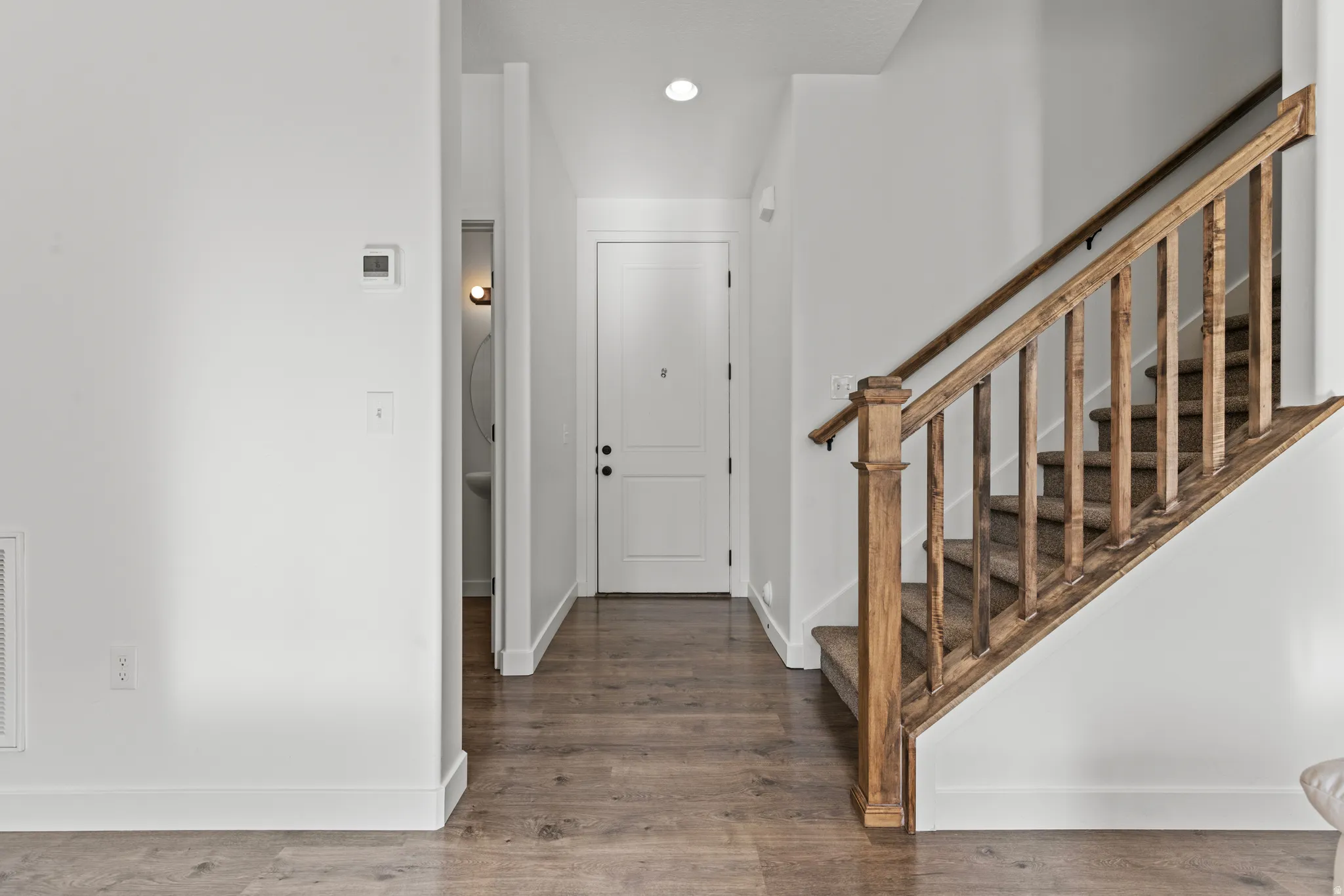 Entryway featuring wood-finish flooring, a wood staircase with carpeted treads, and a modern thermostat