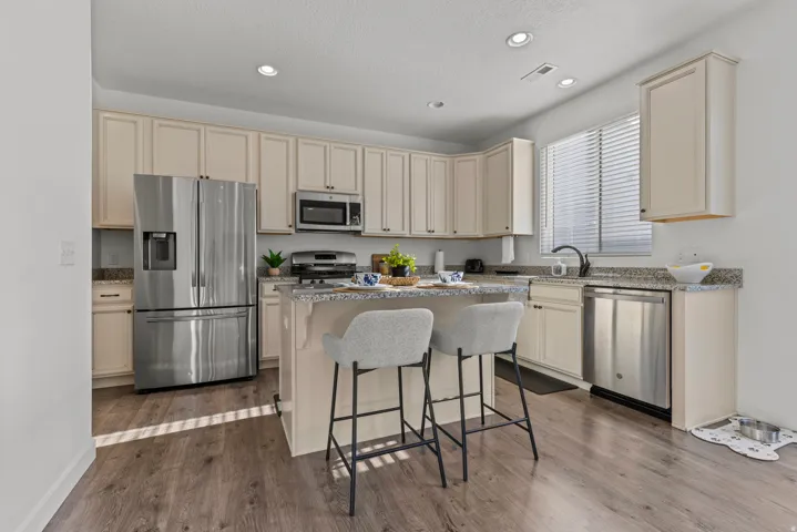 Kitchen featuring light wood-finish cabinetry, granite-style countertops, stainless steel appliances, a center island with built-in seating, and wood-finish flooring