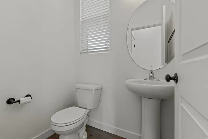 Powder room featuring a pedestal sink with a chrome faucet, an oval mirror, and wood-finish flooring