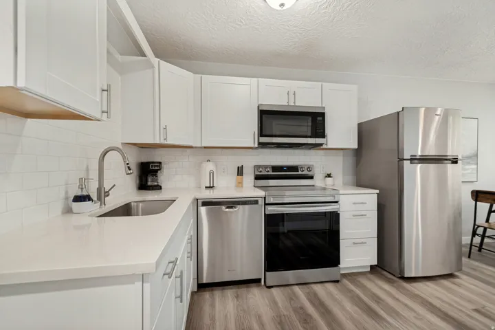 Kitchen featuring white cabinetry, light countertops, stainless steel appliances, a subway tile backsplash, and wood-finish flooring