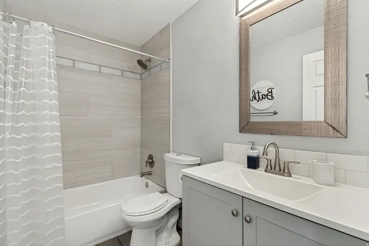 Bathroom featuring a shower-over-tub combination with tile surround, a single vanity with a solid surface countertop, a wood-frame mirror, and brushed nickel fixtures
