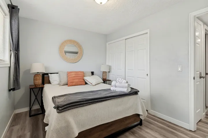 Bedroom featuring wood-finish flooring, a window with blinds, and white bi-fold closet doors