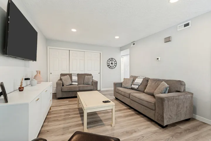 Recessed ceiling lighting illuminates a living area featuring wood-finish flooring, light gray walls, and white bi-fold closet doors
