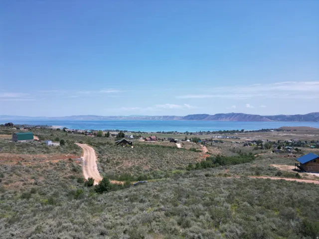 Expansive property featuring a winding dirt road, natural landscaping, and a distant body of water