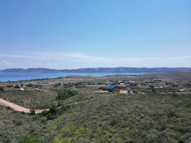 Expansive undeveloped property featuring a dirt road, surrounding hills with scattered homes, and distant water with mountainous terrain