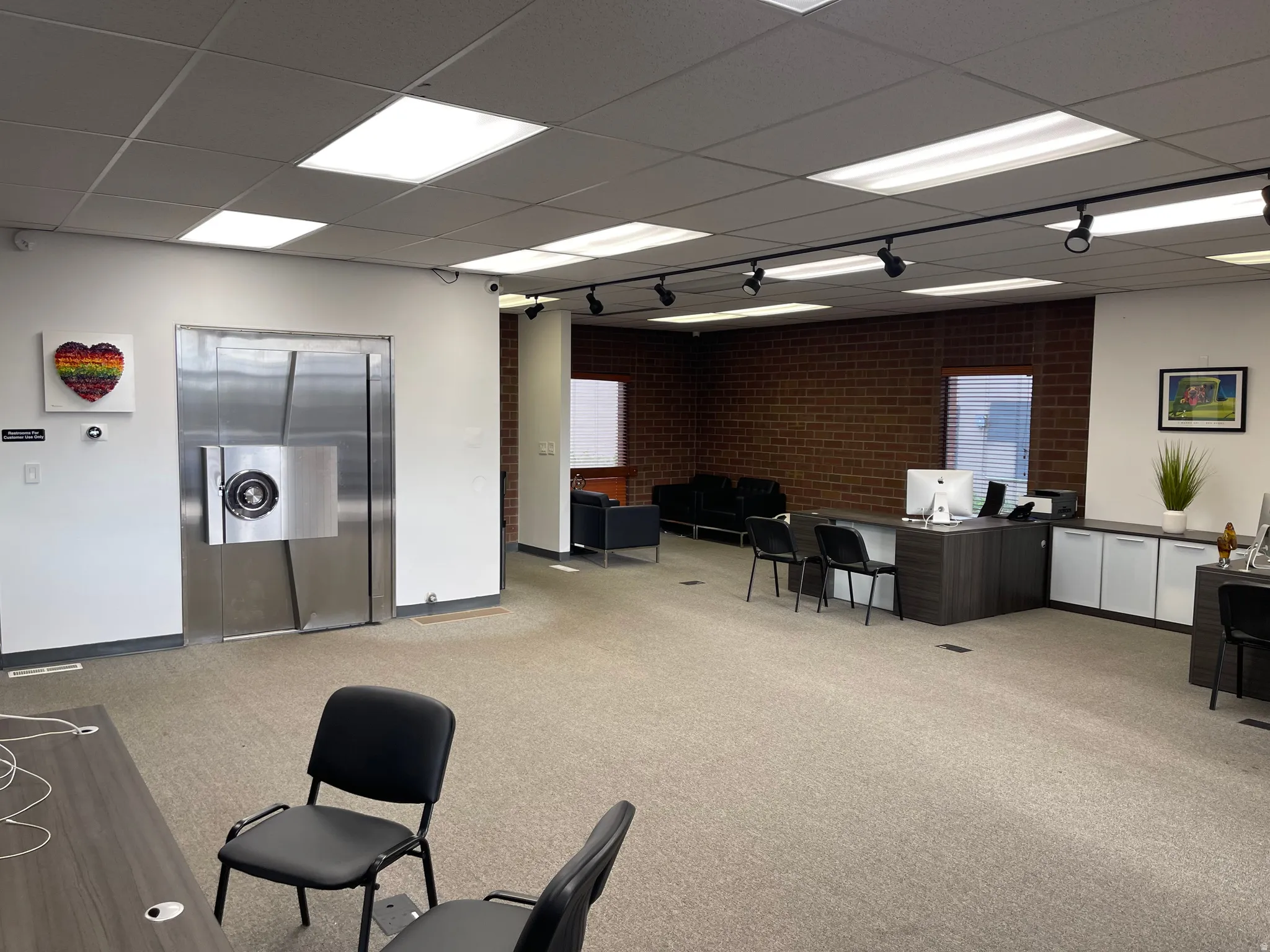 Spacious commercial interior featuring a large vault door, textured brick accent wall, recessed ceiling lighting, track lighting, and soft carpet flooring