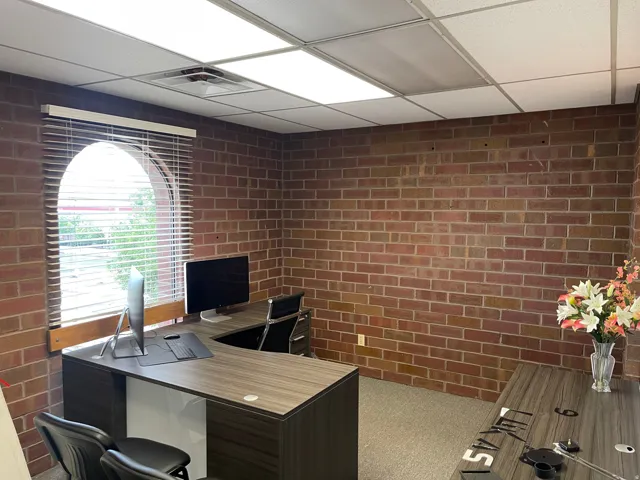 Exposed brick walls complement the arched window with horizontal blinds, providing a distinct architectural detail within this space