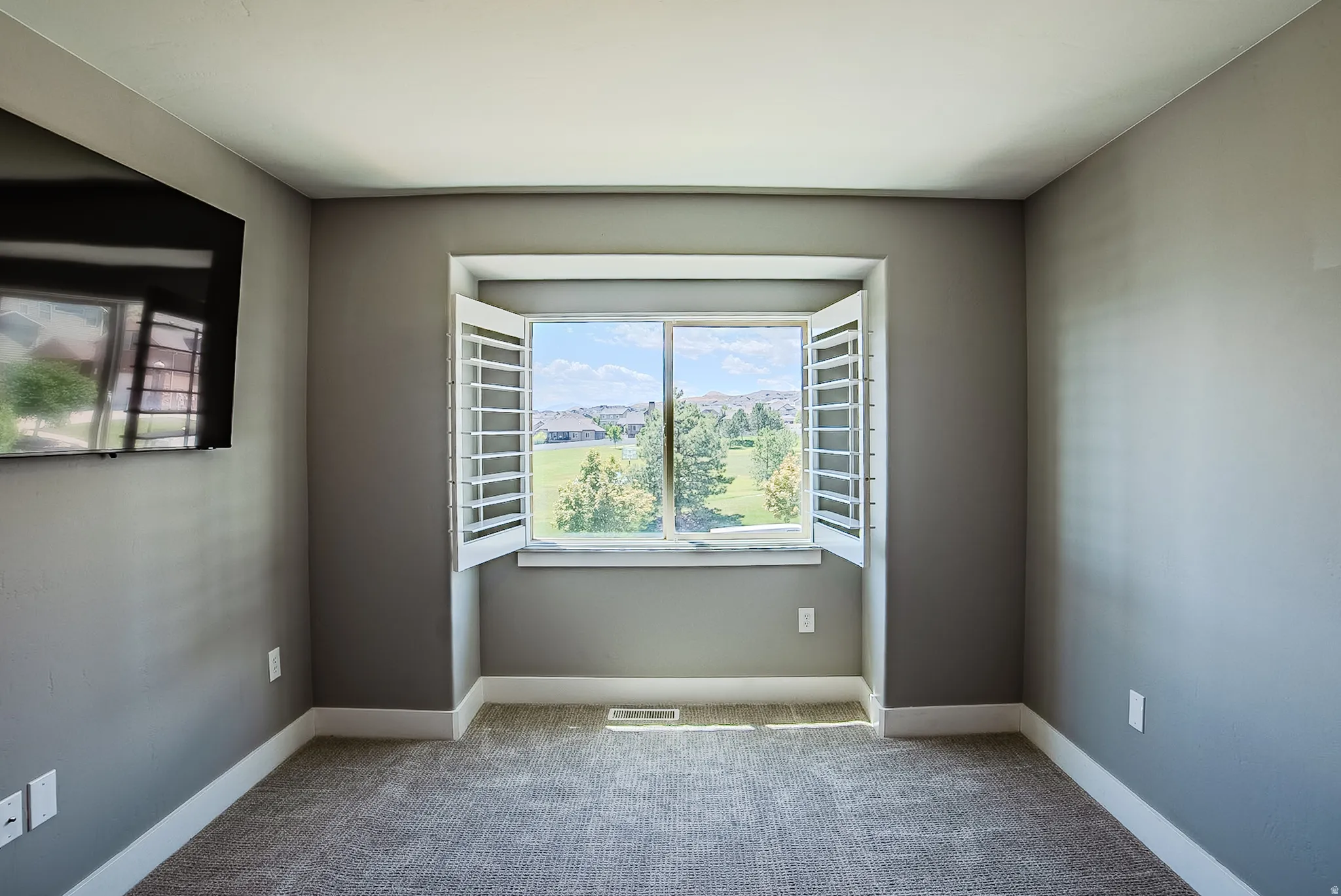 Recessed window with white plantation shutters, gray walls, white trim, and textured carpet flooring