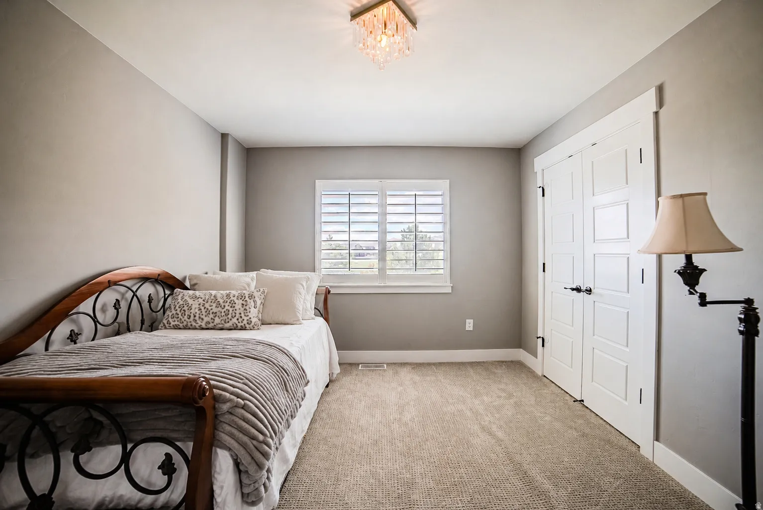 Room featuring neutral wall tones, window with plantation shutters, twin closet doors with dark hardware, a flush-mount crystal chandelier, and textured carpeting