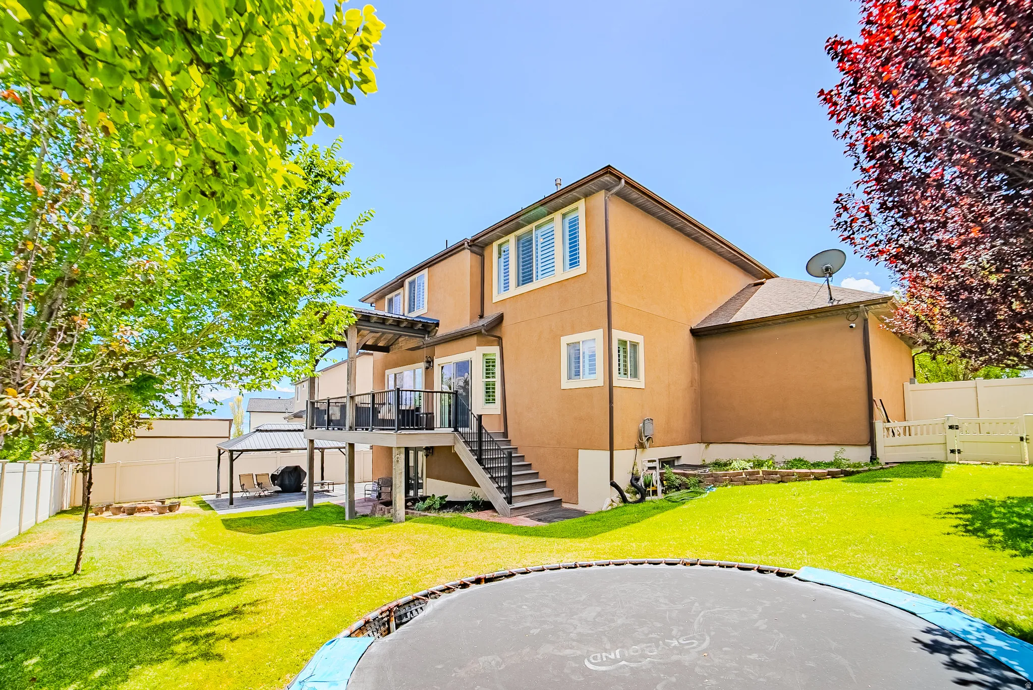 Expansive backyard featuring a manicured lawn, a raised composite deck with black railings and a shaded pergola