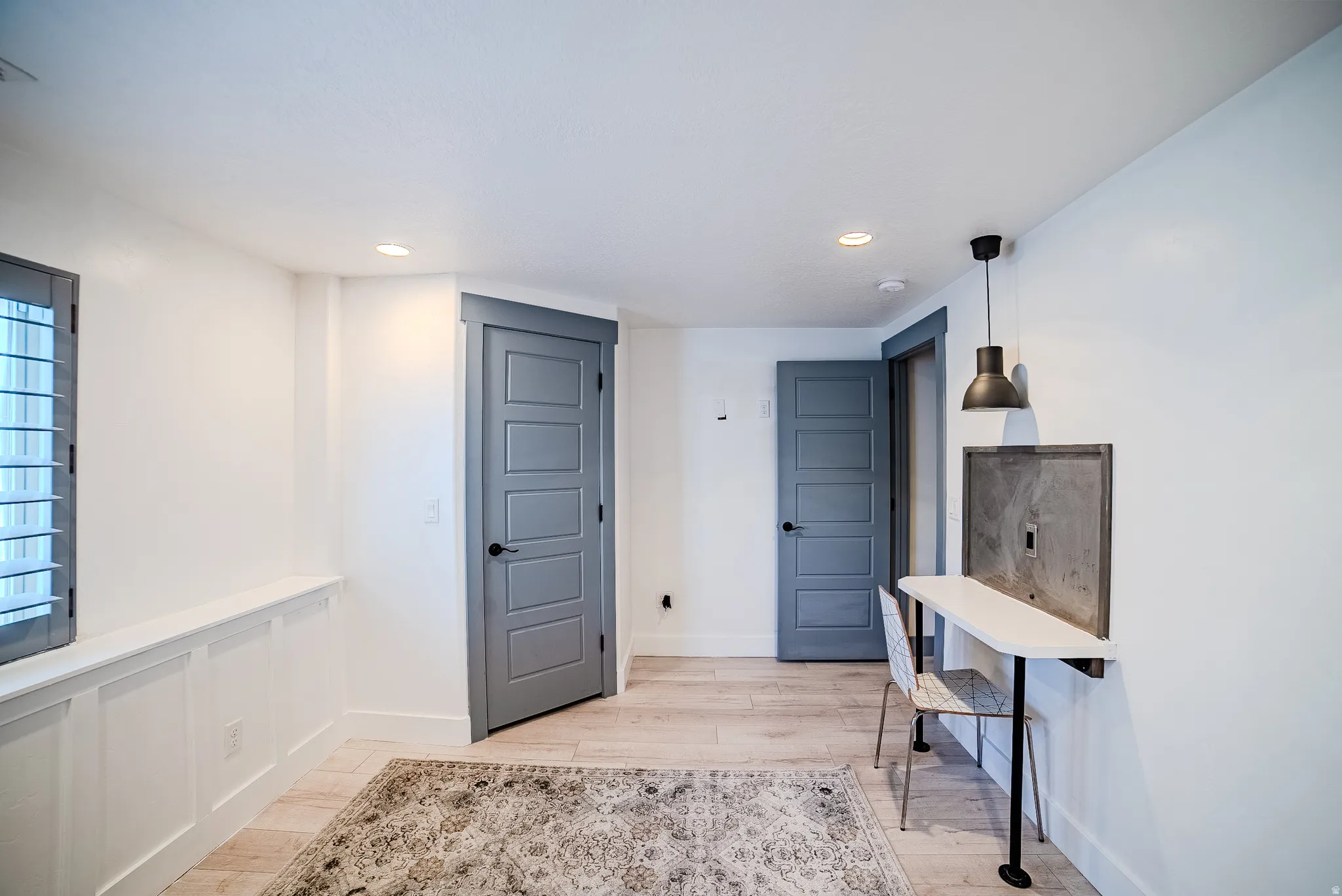 Room featuring light wood-finish flooring, two gray five-panel doors, recessed ceiling lighting, and a window with gray plantation shutters