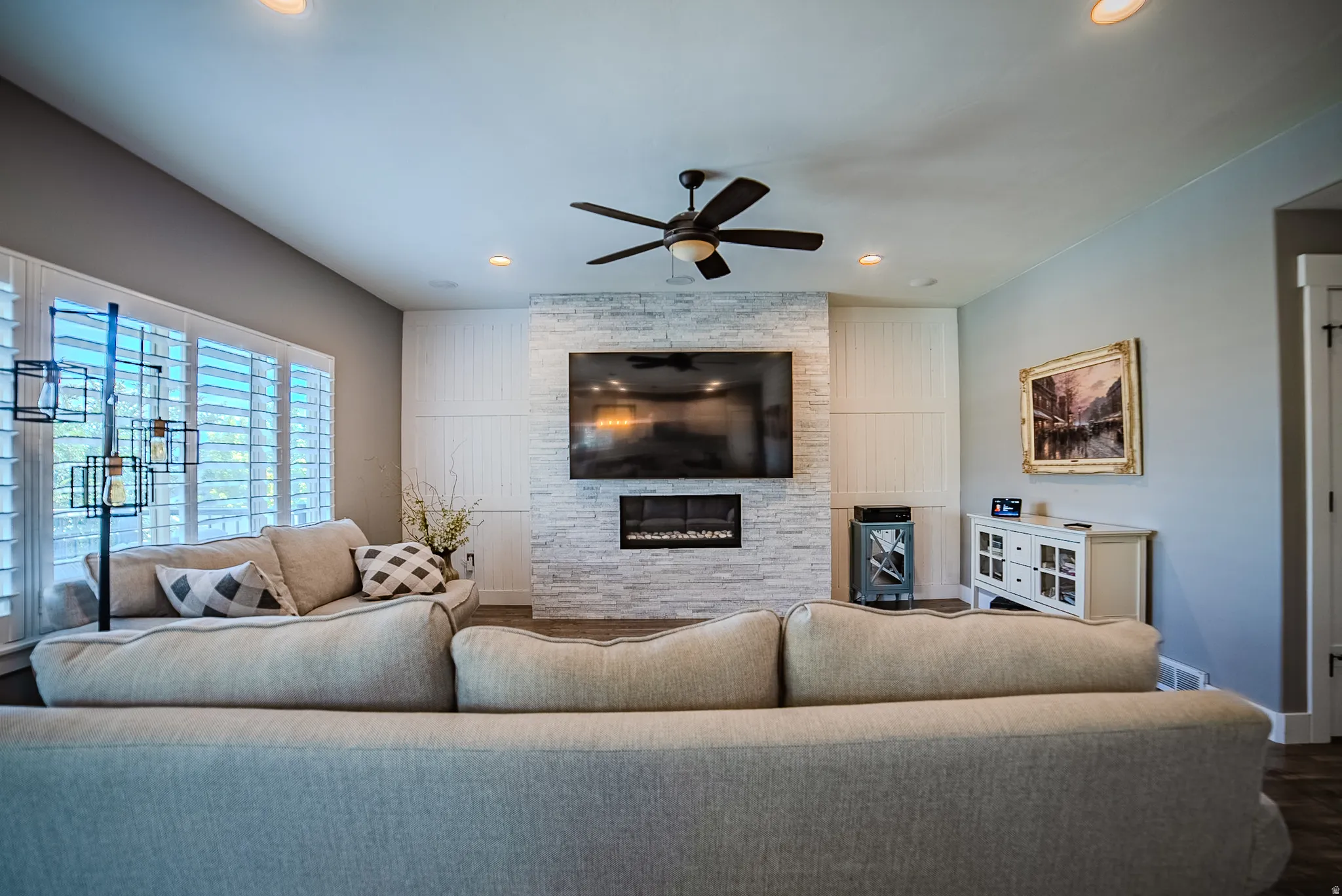 Living area featuring a stone-clad fireplace with an integrated electric insert, a ceiling fan, recessed lighting, plantation shutters, and wood-finish flooring