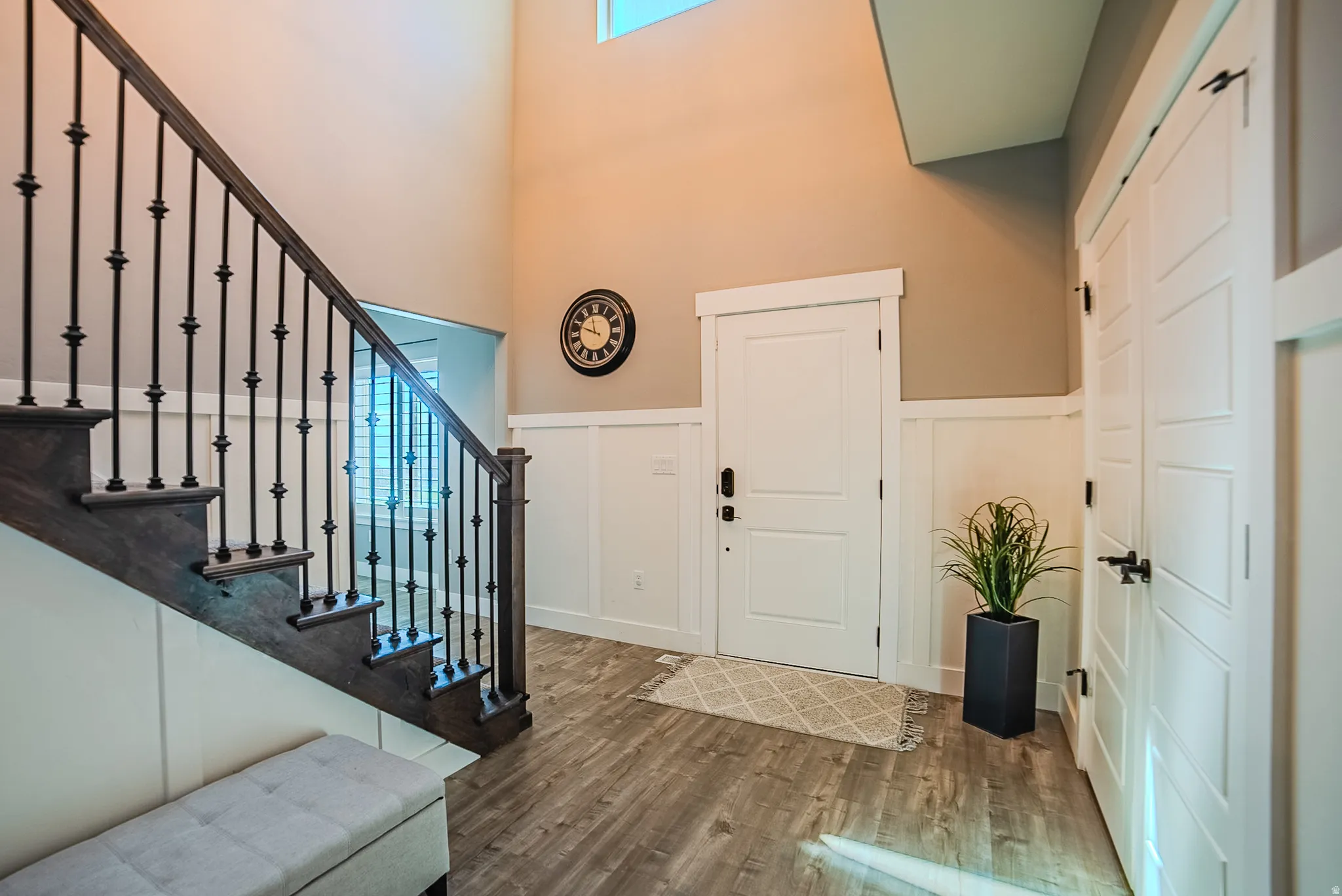 Two-story entryway featuring wood-finish flooring, wainscoting, and a staircase with dark wood treads and iron balusters